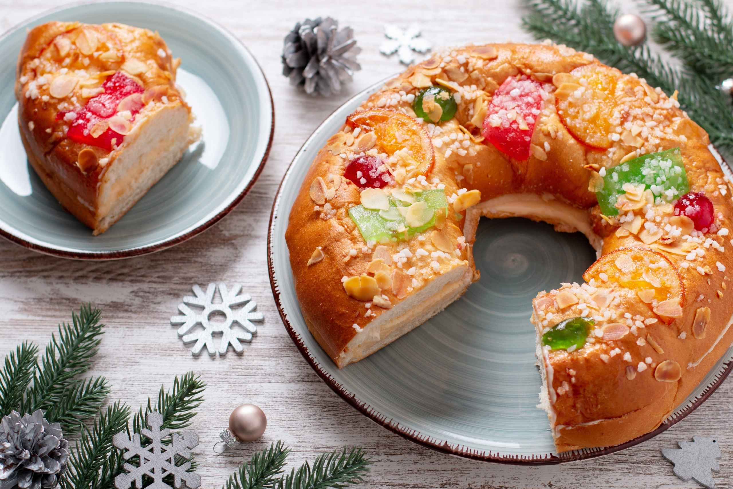 imagen de mesa decorada de navidad con un roscón de reyes que le falta una porción emplatada en otro plato