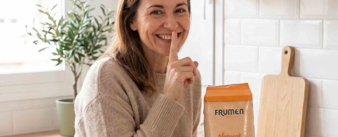 Mujer sonriente mostrando un paquete de pan rallado Frumen, demostrando secretos para lograr platos crujientes y sabrosos en la cocina.